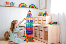 Load image into Gallery viewer, Child playing with a colourful rocket-shaped toy in a room with shelves and storage units.