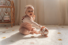 Load image into Gallery viewer, A soft baby toy in the shape of a ball with floral patterns and pink ribbed sections, featuring a label and a small rattle.