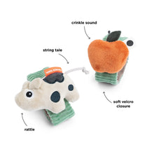 Load image into Gallery viewer, Two plush toys, one resembling a cow and the other an apple, with text labels indicating features like crinkle sound, string tale, soft velcro closure, and rattle.
