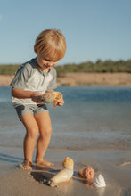 Load image into Gallery viewer, Child playing with shells on a sandy beach
