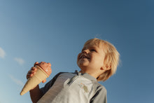Load image into Gallery viewer, Child holding an ice cream cone against a clear blue sky
