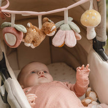 Load image into Gallery viewer, Baby with the stroller toy chain featuring plush toys including a mushroom, a deer, a flower, and a strawberry, attached to a pink strap.
