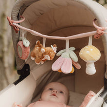 Load image into Gallery viewer, Baby with the stroller toy chain featuring plush toys including a mushroom, a deer, a flower, and a strawberry, attached to a pink strap.
