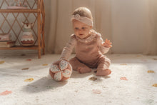 Load image into Gallery viewer, A soft baby toy in the shape of a ball with floral patterns and pink ribbed sections, featuring a label and a small rattle.
