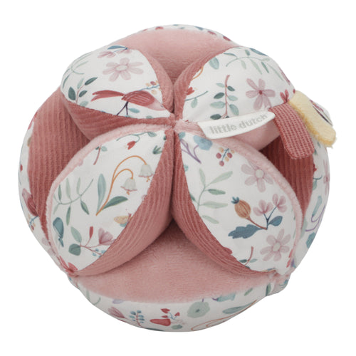 A soft baby toy in the shape of a ball with floral patterns and pink ribbed sections, featuring a label and a small rattle.
