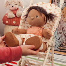 Load image into Gallery viewer, Doll with dark hair and brown shoes held by a hand, sitting in a baby bouncer with a teddy bear in the background.
