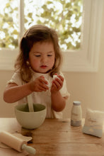 Load image into Gallery viewer, Child playing with a bowl and rolling pin on a wooden table, with a bottle and bag in the background.
