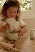 Load image into Gallery viewer, Child playing with a bowl and spoon at a wooden table, with a bottle of milk in the background.

