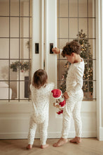 Load image into Gallery viewer, Two children in matching pajamas standing in a room with a Christmas tree in the background and holding Christmas Little dutch Jim doll
