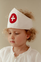 Load image into Gallery viewer, Child wearing a white headband with a red cross symbol on a beige background
