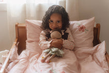Load image into Gallery viewer, Young girl sitting on a bed holding a teddy bear, surrounded by pink bedding and pillows.
