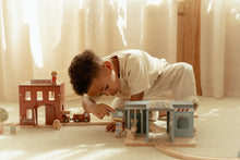 Load image into Gallery viewer, Child playing with toy police station and other toys on a carpeted floor.
