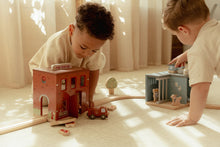 Load image into Gallery viewer, Two children playing with toy fire station and other toys on a light-coloured floor.

