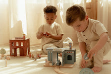 Load image into Gallery viewer, Two young boys playing with toy trains on a wooden floor.
