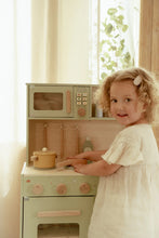 Load image into Gallery viewer, Child playing with a toy kitchen set in a bright room with curtains and plants.
