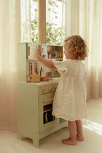 Load image into Gallery viewer, Child playing with a toy kitchen set in a bright room with large windows.
