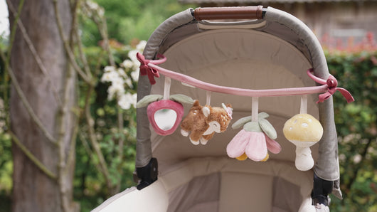 Cot with the stroller toy chain featuring plush toys including a mushroom, a deer, a flower, and a strawberry, attached to a pink strap.