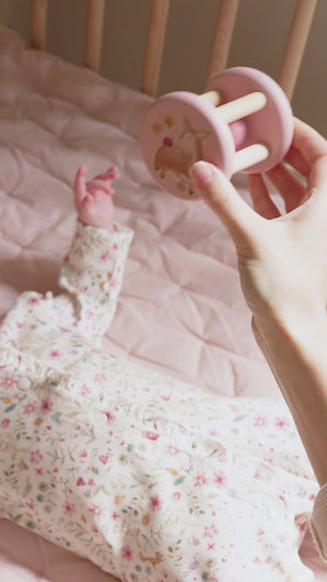 A baby playing with a pink and beige wooden roller rattle toy with a ball in the center and four cylindrical supports. With a pretty image of  deer and a ladybird.