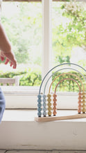 Load and play video in Gallery viewer, A rainbow-shaped abacus with beads in shades of blue and beige, constructed with a wooden base and metal frame.
